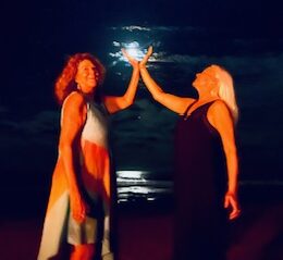 Here's an alt tag for the image: Two women high-five under the moon.