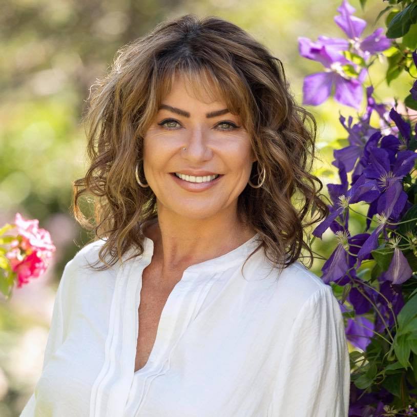 Woman smiling, white shirt, purple flowers.
